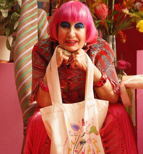 Light skinned fashion designer Zandra Rhodes wearing pink with pink hair holding electrical tote bag she designed